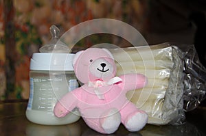 Baby bottle with fresh expresed breast milk, frozen breastmilk in storage bags and soft toy pink teddy bear