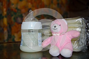 Baby bottle with fresh expresed breast milk, frozen breastmilk in storage bags and soft toy pink teddy bear