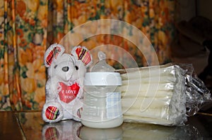 Baby bottle with fresh expresed milk, frozen breastmilk in storage bags and soft toy mouse