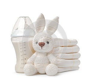 Baby bottle with milk, bunny toy and stack of diapers on white background photo