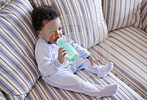 Baby, bottle or sofa for nutrition, health or growth by morning breakfast meal in living room. Hungry, black boy or