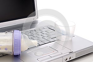 A baby bottle spilling on a notebook computer