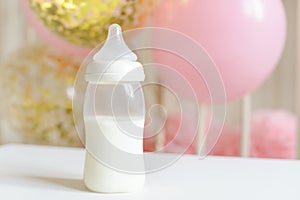 Baby bottles with breast milk with various festive paper decor and balloons in front of baby bedroom. It`s a girl or baby birthda