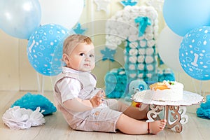 Baby boy 1 year in a photo Studio with a cake and balloons, Birthday of a child 1 year, baby eats cake