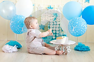 Baby boy 1 year in a photo Studio with a cake and balloons, Birthday of a child 1 year, baby eats cake