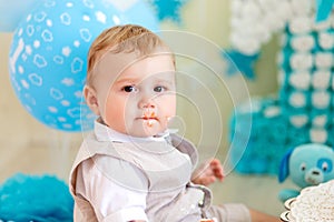 Baby boy 1 year in a photo Studio with a cake and balloons, Birthday of a child 1 year, baby eats cake