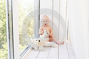 Baby boy 8 months old lying in diapers on a white bed with a bottle of milk at home legs up, top view, baby food concept, baby