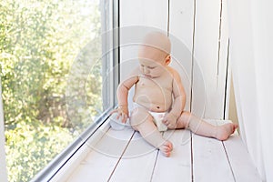 Baby boy 8 months old lying in diapers on a white bed with a bottle of milk at home legs up, top view, baby food concept, baby