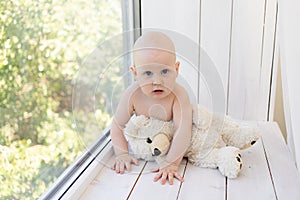 Baby boy 8 months old lying in diapers on a white bed with a bottle of milk at home legs up, top view, baby food concept, baby