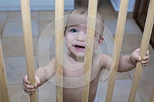 Baby boy behind the wooden safety gate of stairs