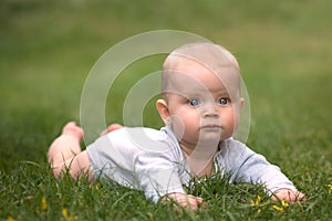 Baby boy with big blue eyes is lying on green grass and