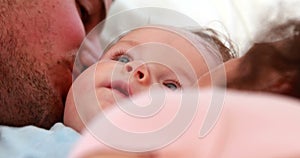 Baby boy in blue babygro being kissed by happy parents on bed