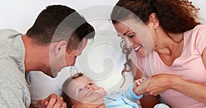 Baby boy in blue babygro being tickled by happy parents on bed