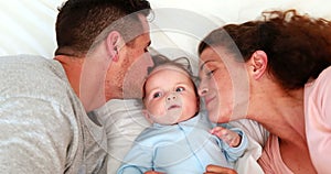 Baby boy in blue babygro with happy parents on bed