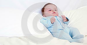 Baby boy in blue babygro lying on pillows