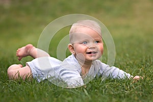 Baby boy with blue eyes is lying on green grass and smiling