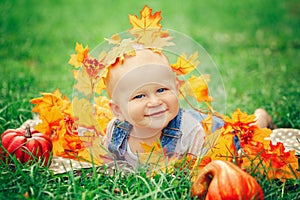 Baby boy with blue eyes in t-shirt and jeans romper lying on grass field meadow in yellow autumn leaves