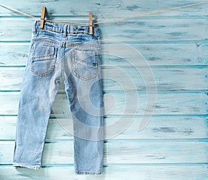 Baby boy blue jeans hanging on a clothesline on blue wooden background