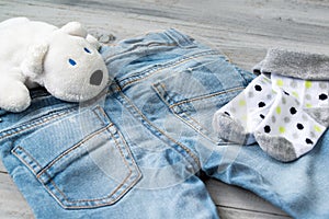 Baby boy blue jeans, socks and white toy bear on a wooden background