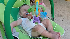 Baby boy in bouncer puting fingers in his mouth