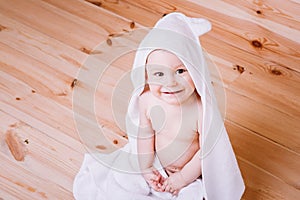 Baby boy with brown eyes is five months old wrapped in a white towel with ears on wooden background .