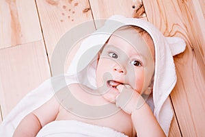 Baby boy with brown eyes is five months old wrapped in a white towel with ears on wooden background .