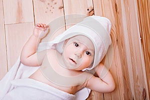 Baby boy with brown eyes is five months old wrapped in a white towel with ears on wooden background .