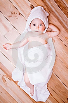 Baby boy with brown eyes is five months old wrapped in a white towel with ears on wooden background .