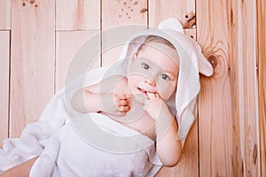 Baby boy with brown eyes is five months old wrapped in a white towel with ears on wooden background .