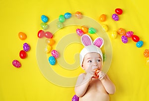 Baby boy in bunny hat lying on yellow blanket with easter eggs