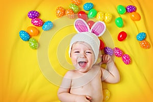 Baby boy in bunny hat lying on yellow blanket with easter eggs