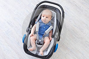 Baby boy in car seat, happy newborn lying strapped in seatbelt