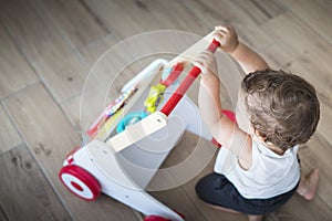 Baby boy playing with walking toy. Top view, indoor