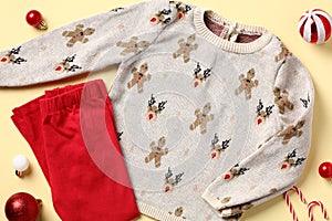 Baby boy clothes Christmas outfits top view. Flat lay red pants, sweater and Xmas decorations on yellow background