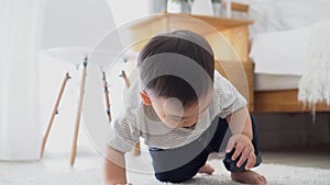 Baby boy crawling on the floor in living room indoors. Toddler Asian family at home