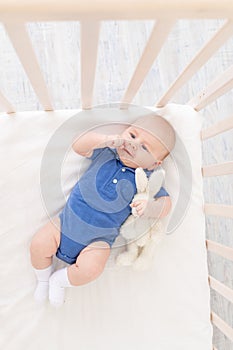 A baby boy in a crib lies on his back, a happy newborn wakes up in the morning or goes to bed