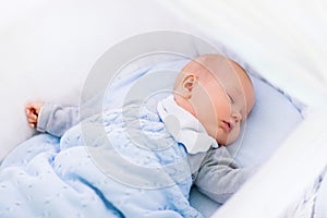 Baby boy in a crib under knitted blanket