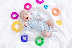 Baby boy crying on bed among toys