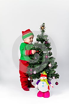 Baby boy dressed as Santa's Helper decorating Christmas tree.