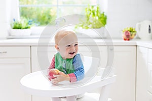 Baby boy eating apple in white kitchen at home