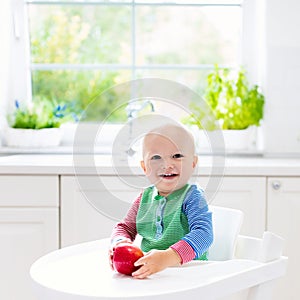 Baby boy eating apple in white kitchen at home