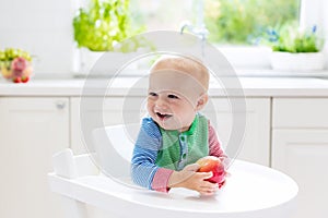 Baby boy eating apple in white kitchen at home