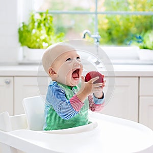 Baby boy eating apple in white kitchen at home