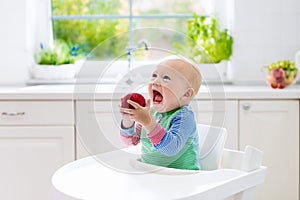 Baby boy eating apple in white kitchen at home