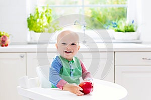 Baby boy eating apple in white kitchen at home