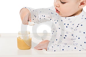 baby boy eating puree from jar and sitting in highchair