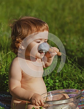 Baby boy eating vegetable mash outdoor on green grass. Carefree childhood in village.