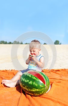 Baby boy eating watermelon slice against beach background