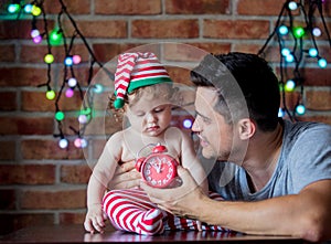 Baby boy in elf hat and father with alarm clock