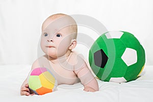 Baby boy or girl lying down on his belly and playing with soccer balls